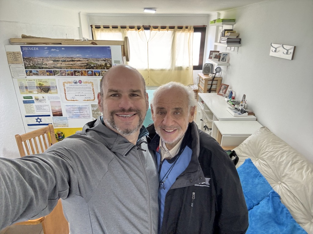 Mauro y Mario reunidos en la casa de Mario, con parte de sus libros y documentos en la pared, el 11 de septiembre de 2024